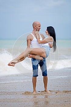 Man carrying her wife along wet sand in time of surf