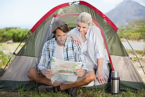 Attractive couple sitting by their tent reading map