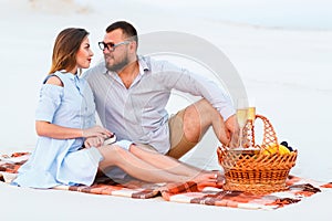 Attractive couple sitting together on the white sand beach, looking each other, happy couple enjoying picnic on the beach and have