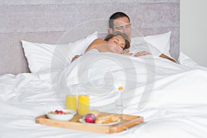 Attractive couple sleeping with breakfast tray on bed