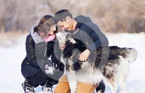 Attractive couple smiling and having fun in winter park with their husky dog