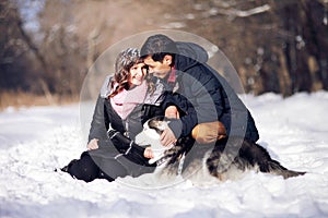 Attractive couple smiling and having fun in winter park with their husky dog