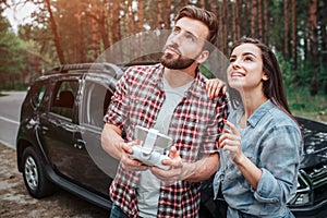 Attractive couple is standing together and looking up. They are ouside in park. There is a car behind them. Guy is