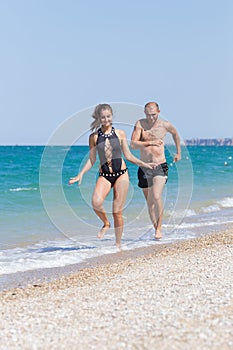 Attractive couple in swimwear running along seashore