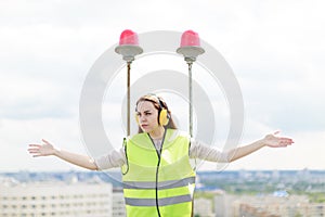 Attractive cute worker woman in green west and earmuffs stand on roof, hold tablet