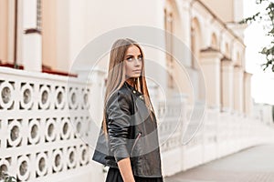 Attractive cute young woman model with beautiful natural make-up in a vintage black leather jacket with brown hair posing outdoors