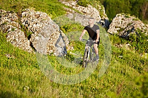 Attractive cyclist riding bike on the meadow with stones in the countryside.