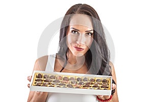 Attractive dark-haired woman happily holding a candy box full of chocolate. Isolated background