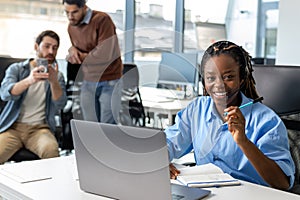 Attractive dark skinned woman in headset working on laptop