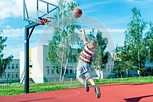 Attractive east european caucasian little basketball player jumps to throw the ball into the hoop.outdoors red court