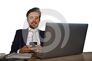 Attractive and efficient business man working at office laptop computer desk confident in smiling happy using mobile phone in succ