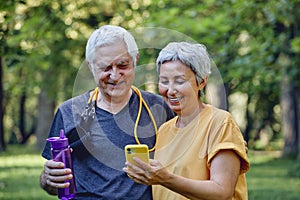 Attractive elderly spouses using modern smartphone after sportive work out