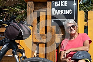 Attractive elderly woman on excursion with her bicycle stops at aperitif bar with parking area for cyclists