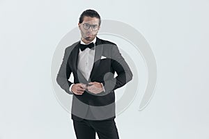 attractive elegant man with glasses closing and buttoning black tuxedo