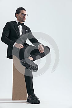 attractive elegant man looking to side while sitting with ankle on knee