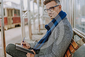 Attractive elegant man writing in notebook outdoors