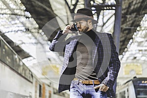 Attractive elegant young hispanic man holding smart phone in his hand and calling while he standing at the railway