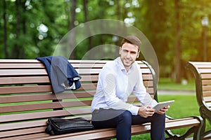 Attractive enterpreneur with tablet taking break on bench in green park