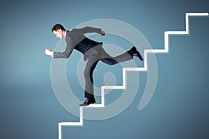 Attractive european businessman running down on abstract stairs on grey background. Financial trouble concept