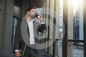 Attractive european businessman in suit drinking coffee near office building during break
