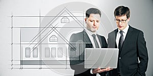 Attractive european businessmen using laptop with abstract drawing of creative house project blueprint on white background.