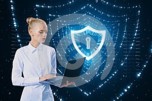 Attractive european businesswoman using laptop with glowing polygonal web security shield hologram on blurry background. Digital