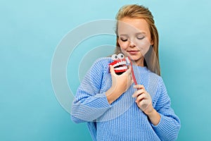 Attractive european girl holds a toothbrush and jaw in her hands on a light blue wall with copyspace