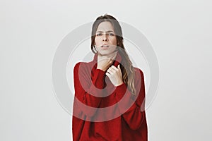 Attractive european woman in stylish red sweater having sore throat feeling pain after catching cold, isolated over