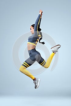 Attractive excited fitness girl dancer in sportwear jumping of joy isolated over gray background