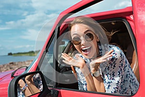 attractive excited girl in sunglasses gesturing and sitting in car