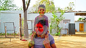 Attractive facial shot of young adult with red smeared color. Indian father and little kid on festival of Holi