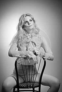 Attractive fair hair model with in elegant nude blouse sitting provocatively on chair, studio shot. Fashion portrait