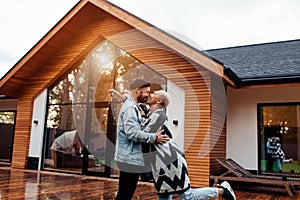 Attractive family of wife and husband kissing next to big wooden house