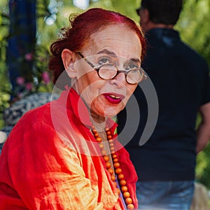 Attractive fashionable woman of 75 in red clothes sitting and roundly eyeglasses in a summer park