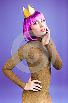 Attractive fashionable young woman in stylish luxury dress, cut pink hair on violet background. Brightful makeup with