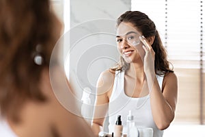 Attractive Female Applying Cream Moisturizer On Skin In Bathroom Indoors