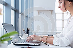 Attractive female assistant working, typing, using portable computer, concentrated, looking at the monitor. Office