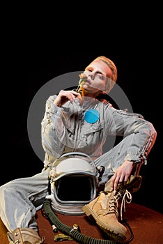 attractive female astronaut in spacesuit with helmet sitting on planet and holding