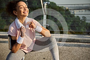 Attractive female athlete, delightful sports women sitting on squat pose on the city glass bridge, holding a white terry towel
