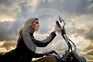 Attractive female brunette motorcyclist with motorcycle in a summer evening during sunset. Beautiful girl with a bike on