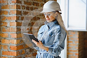 Attractive female construction worker in hardhat. Confident young specialist in checkered blue shirt in jeans standing