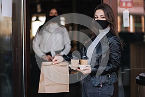 Attractive female customer in face mask standing outdoors by cafe and take away food and coffee. Background of cashier