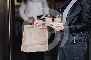 Attractive female customer in face mask standing outdoors by cafe and take away food and coffee. Background of cashier