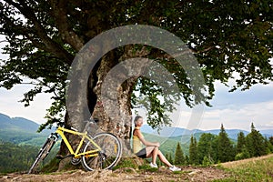 Attractive female cyclist with yellow mountain bicycle, enjoying sunny day in the mountains