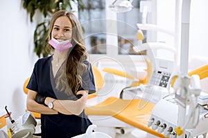 Attractive female dentist doctor standing in her office, looking at the camera