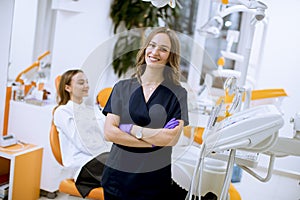 Attractive female dentist doctor standing in her office, looking at the camera