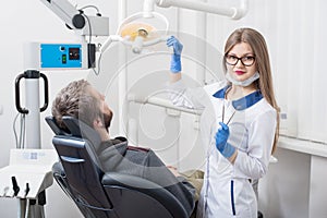 Attractive female dentist getting ready for dental procedure with male patient in modern dental office