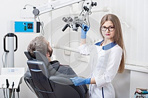 Attractive female dentist with microscope getting ready for dental procedure with male patient in modern dental office