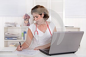 Attractive female doctor working at desk with laptop.