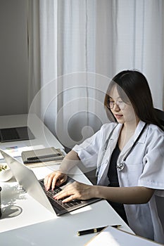 Female doctor is working with documents and laptop in her medical office.